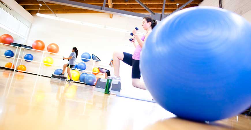 Two women holding hand weights exercise inside a gym.