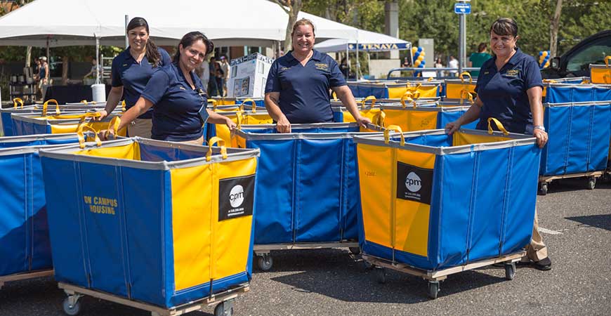 Four UC Merced employees pose with blue and gold moving bins.