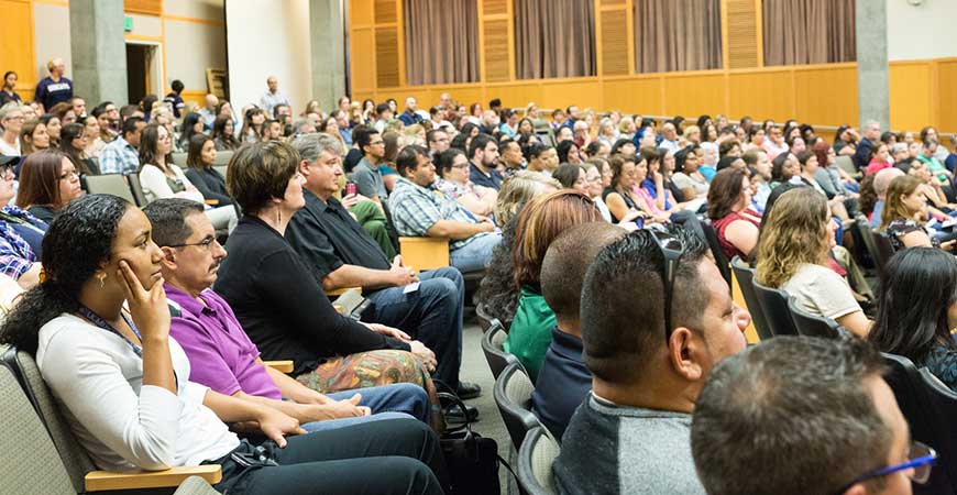 Several hundred staff members are seated in the Dr. Lakireddy Auditorium listening to a speaker on stage.