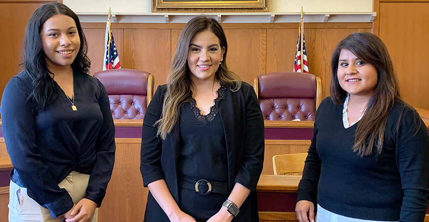 Three women stand next to each other in a mock courtroom.