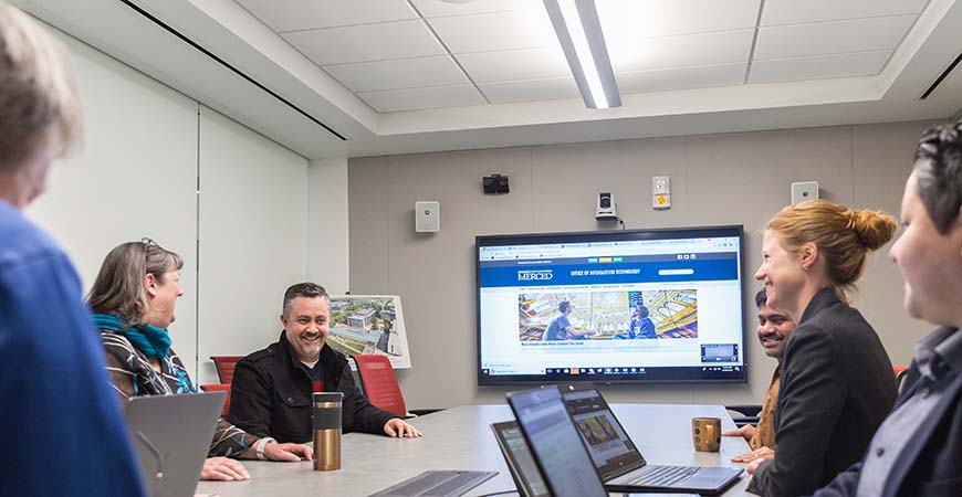 employees cheerfully gathered around a conference table with computers