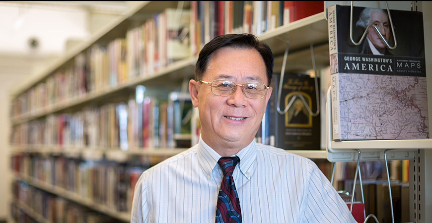 University Librarian Haipeng Li stands next to book shelves in the UC Merced Library