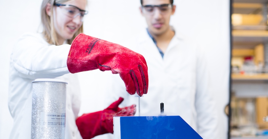 Two students in white lab coats work in a chemistry lab.