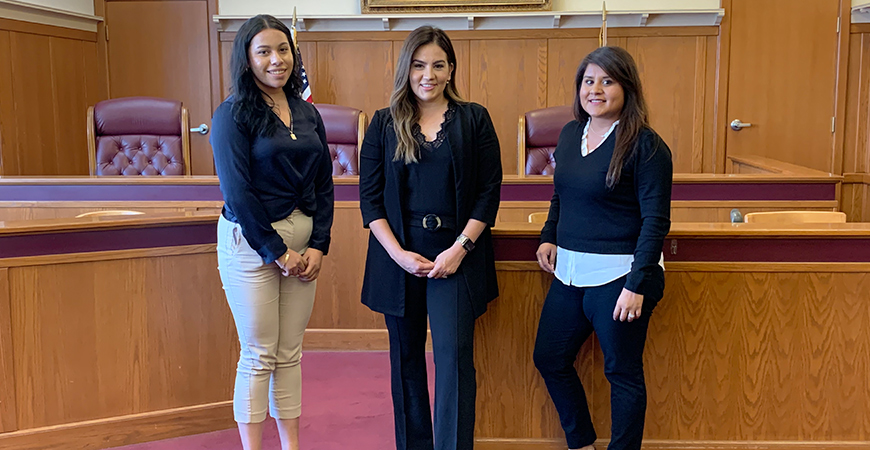 Three women stand next to each other in a mock courtroom.