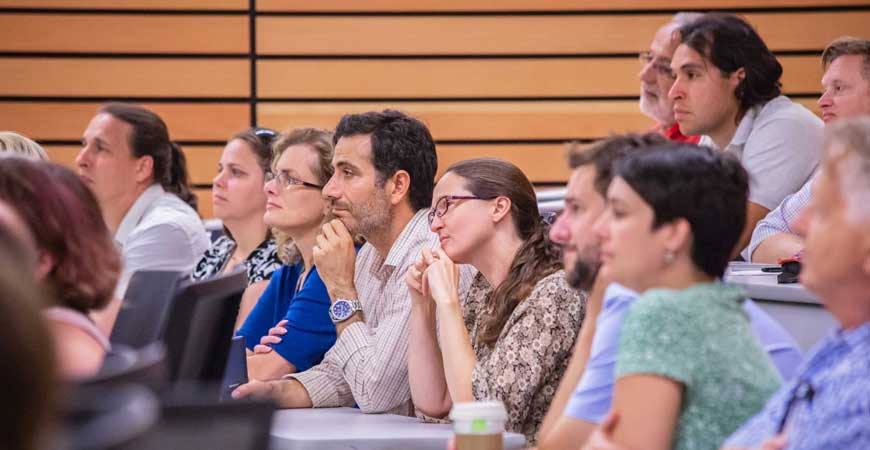 Faculty members listen to a presentation inside a large classroom.