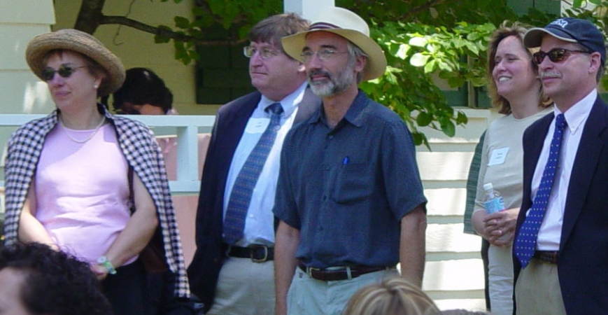 Five adults in professional attire listening to a speaker