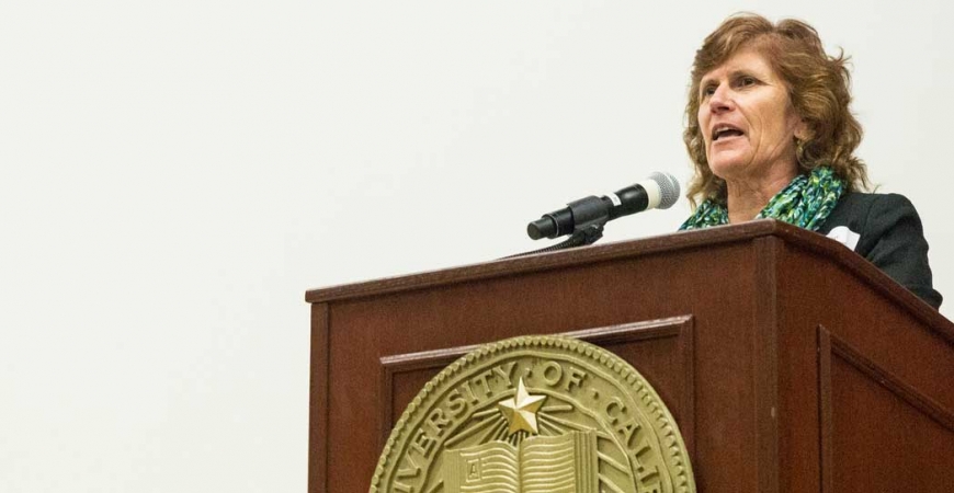 De Acker, director of the Office of Campus Climate, stands at a lectern while addressing an audience.