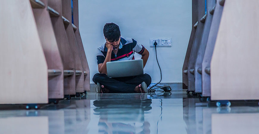 Young man sitting against the wall with head down and laptop computer open on lap