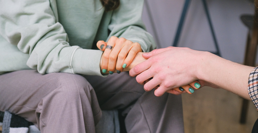 A woman comforts another woman by holding her hand.